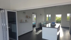 A modern kitchen with a central island, a dining area with a sofa, and a sliding glass door leading to a balcony.