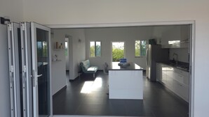 A modern kitchen with a central island, a dining area with a sofa, and a sliding glass door leading to a balcony.