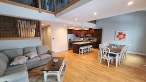 A spacious living area with a sofa, coffee table, and dining table with chairs. A kitchen is visible in the background with modern appliances.