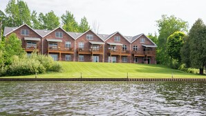 A row of brick buildings with balconies, a grassy area in front, and a body of water.