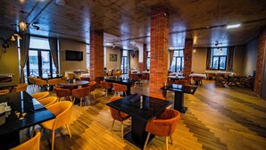 Ein geräumiges Restaurant mit hohen Decken, freiliegenden Backstein-Säulen und Holzböden. Tische und Stühle sind zum Essen angeordnet.