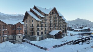 Ein mehrstöckiges Hotel mit Blick auf ein Skigebiet, mit einem zentralen Gebäude mit Balkonen und einer Gondelbahn.