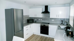 Una cucina moderna con mobili bianchi, un frigorifero in acciaio inossidabile, un forno a microonde, una lavastoviglie e un lavello.