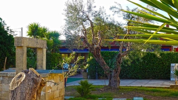 A stone structure in a garden with trees and a building in the background. - B&B Sant'Antonio (Gallipoli)