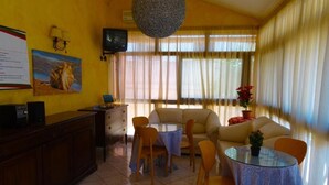 A cozy room with a sofa, two dining tables, a TV, and a large window with curtains. - B&B Sant'Antonio (Gallipoli)