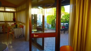 A room with a sliding glass door leading to an outdoor patio area. Inside, there is a round table with chairs, a sofa, and a small table with a vase. - B&B Sant'Antonio (Gallipoli)