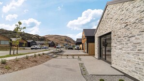 A modern building with a stone facade, a parking area with cars, and a hilly landscape in the background. - Close to the remarkable ski field, modern and warm. (Queenstown)