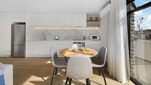 A modern kitchen with white cabinetry, a stainless steel refrigerator, a wooden dining table with grey chairs, and a view of the outside through a large window. - Close to the remarkable ski field, modern and warm. (Queenstown)