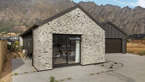 A stone building with a large glass door, a small attached garage, and a mountain backdrop. - Close to the remarkable ski field, modern and warm. (Queenstown)