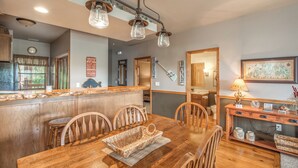 A kitchen with wooden cabinets, a dining table with chairs, and a hanging light fixture. - 2BR Village At Indian Point 1306 near SDC - Free Tickets Daily up to $500 (Branson)
