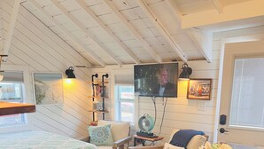 A cozy, well-lit room with a bed, a small table, a bar area, and a television. - Lovely studio steps to the beach in Dennis port (Dennis)