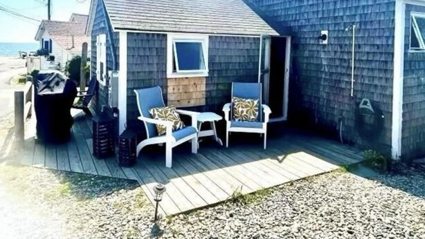 A small, single-story house with a porch, two chairs, and a small table. - Lovely studio steps to the beach in Dennis port (Dennis)