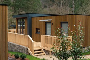 Situated in a natural setting, this compact building features a deck area with a wooden ramp and fence.