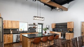A spacious kitchen with wooden cabinets, a large island with bar stools, and a hanging light fixture. - 5 King Beds | Sleeps 18 | Pickleball | Brew Trail (Nelson County)