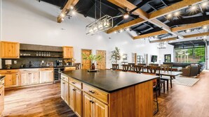A spacious kitchen with wooden cabinets, a large island, and a dining area with a view of the outdoors. - 5 King Beds | Sleeps 18 | Pickleball | Brew Trail (Nelson County)