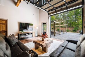 A modern living room with a large TV, comfortable seating, and a view of the outdoor patio. - 5 King Beds | Sleeps 18 | Pickleball | Brew Trail (Nelson County)