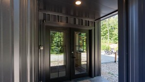 A modern building entrance with a dark exterior, large glass doors, and a visible outdoor seating area with tables and chairs. - 5 King Beds | Sleeps 18 | Pickleball | Brew Trail (Nelson County)