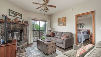 A living room with a stone fireplace, a sofa, a coffee table, and a ceiling fan.