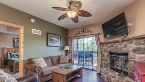 A living room with a stone fireplace, a ceiling fan, and a television mounted on the wall. - 1BR Village At Indian Point 902 near SDC-Free Tickets Daily up to $500 Value (Branson)