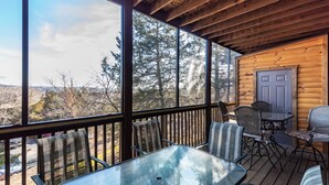 Une terrasse en bois avec des tables et des chaises en verre, donnant sur une zone boisée.