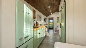 Una cocina estrecha con techo de madera, refrigerador verde y encimera de madera.