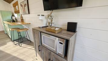 Una cocina con microondas, cafetera y un televisor montado en la pared.