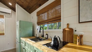 Una cocina con un refrigerador verde, una encimera de madera, una tetera negra y una tabla de cortar de madera.