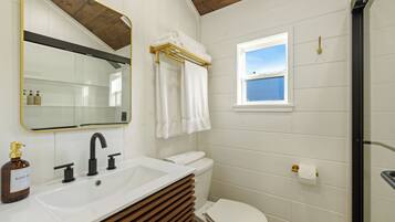 A bathroom with a white sink, black faucet, and a toilet. There is a window with a view of the sky, and a towel rack with towels.