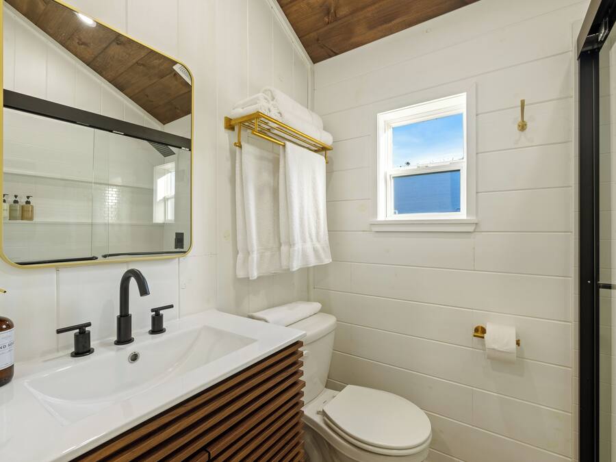 A bathroom with a white sink, black faucet, and a toilet. There is a window with a view of the sky, and a towel rack with towels.