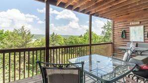 Une terrasse en bois avec une table et des chaises en verre, donnant sur un lac et une forêt.
