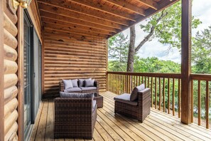A log cabin with a wooden deck, wicker furniture, and a view of trees.