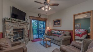 A living room with a stone fireplace, leather sofas, a ceiling fan, and a television mounted above the fireplace.