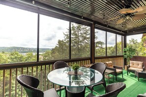 A glass table with wicker chairs, a ceiling fan, and a view of trees and a river.