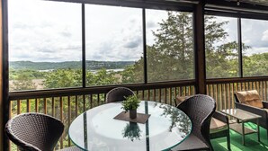 Een tafel met glazen blad, rieten stoelen en uitzicht op een landschap door grote ramen.