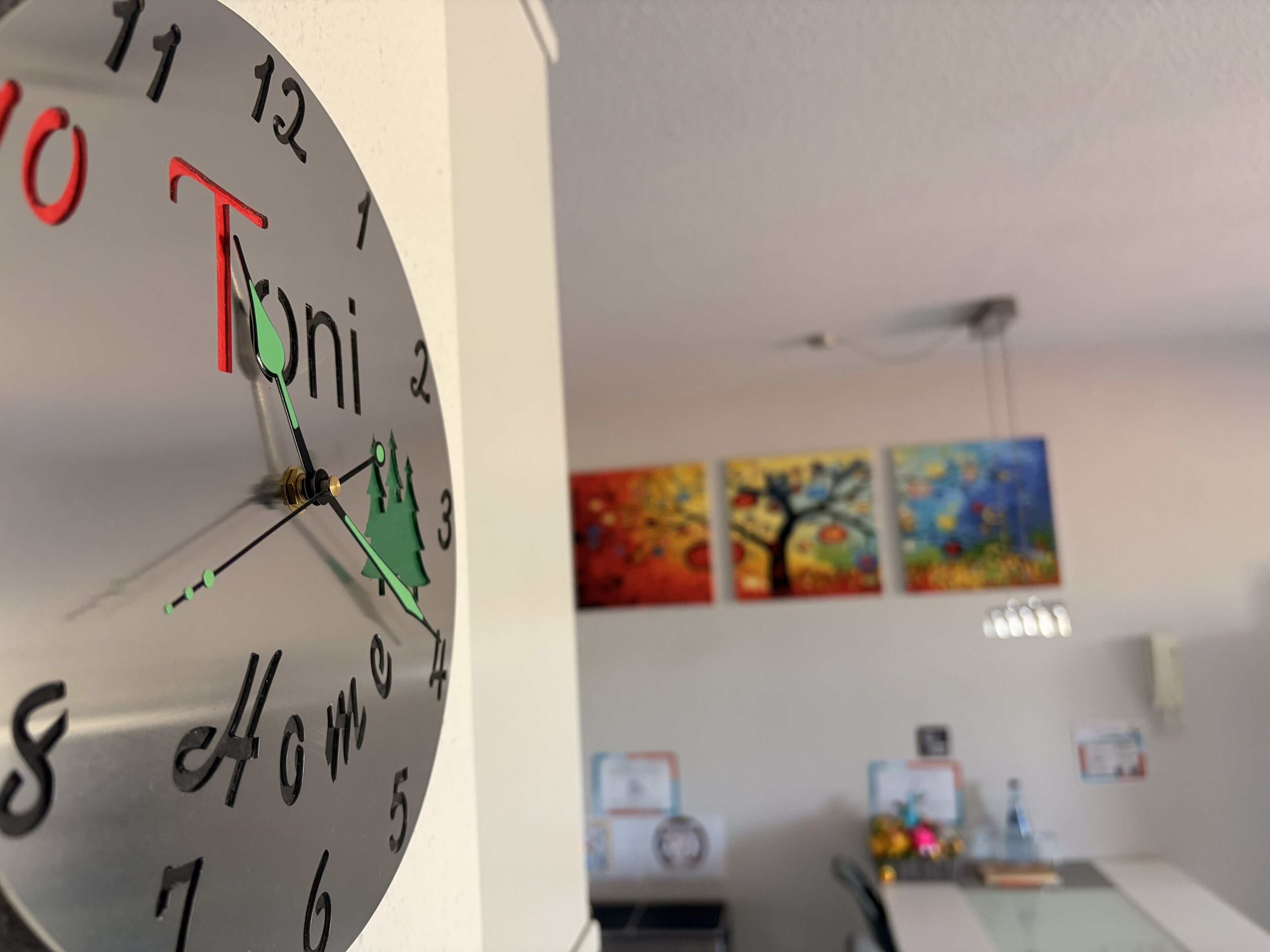 A clock with a unique design, a wall with framed artwork, and a ceiling fan.