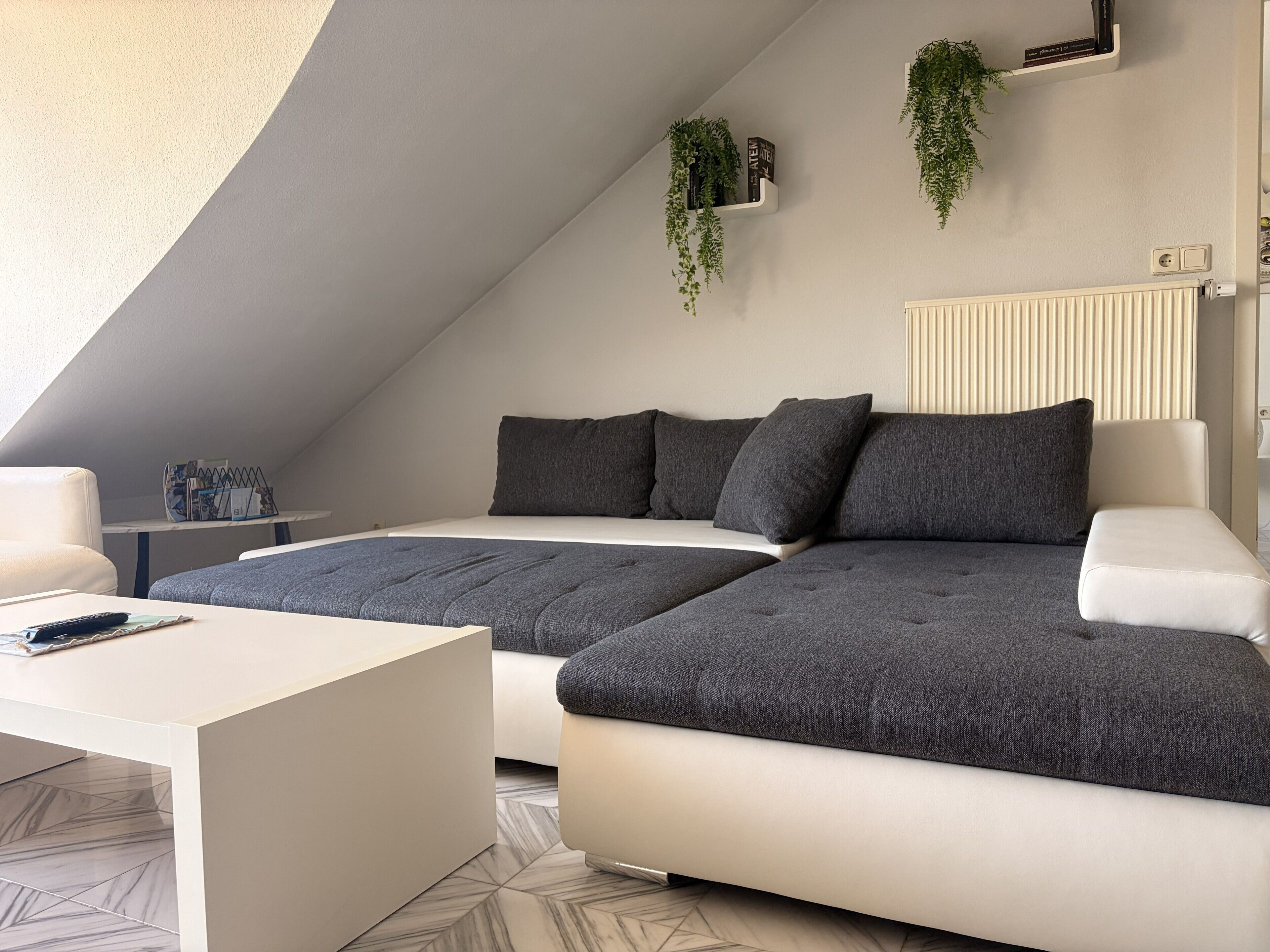 A modern loft bedroom with a large bed, a sofa, a coffee table, and a radiator.