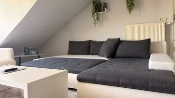 A modern loft bedroom with a large bed, a sofa, a coffee table, and a radiator.