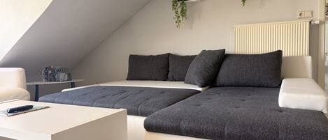 A modern loft bedroom with a large bed, a sofa, a coffee table, and a radiator.