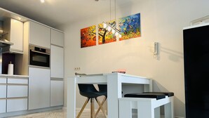 Une cuisine moderne avec des armoires blanches, un four encastré et un coin repas comprenant une table blanche et des chaises noires.
