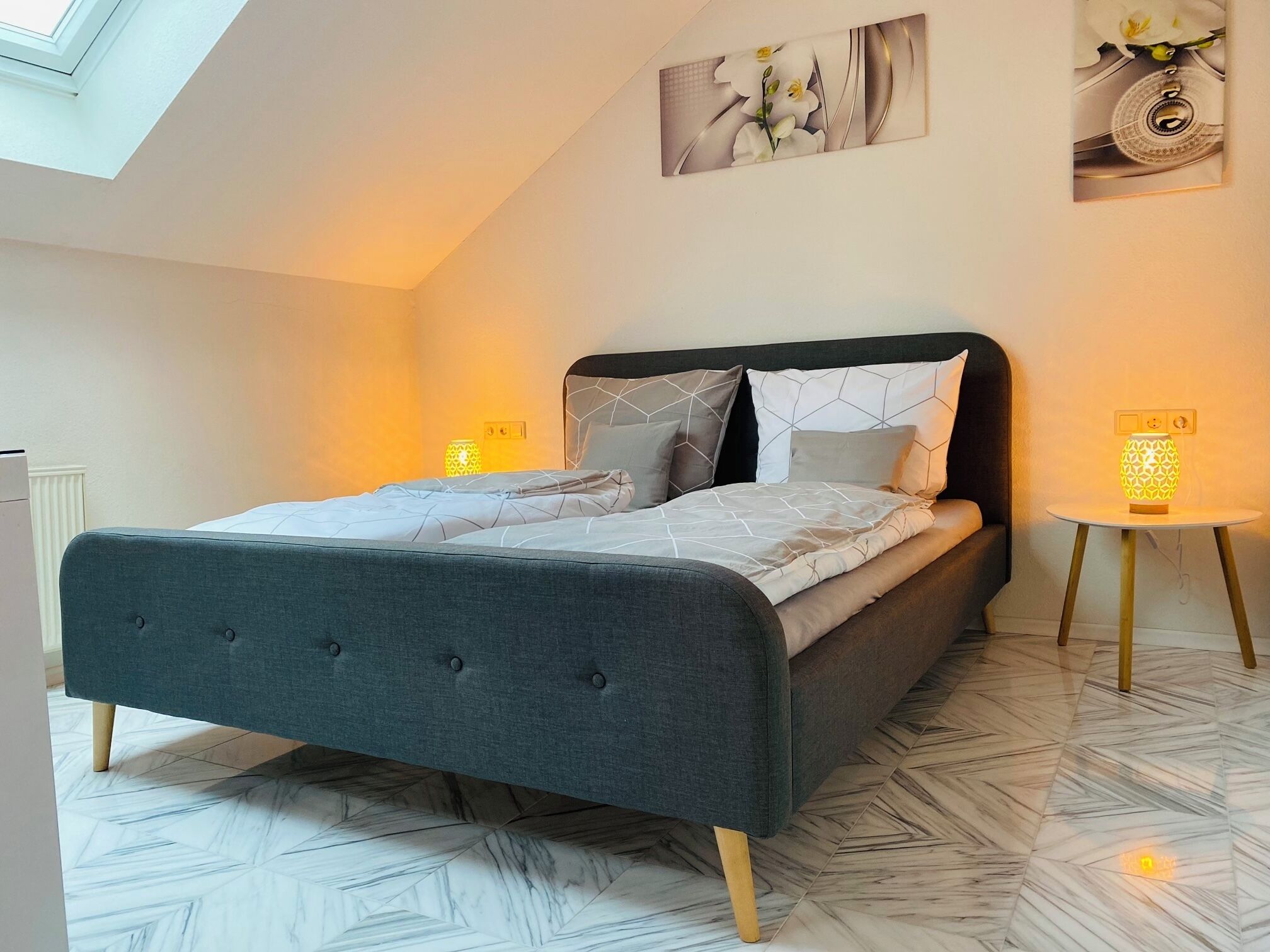Een moderne slaapkamer met een bed, een klein nachtkastje, een wandlamp en een dakvenster.