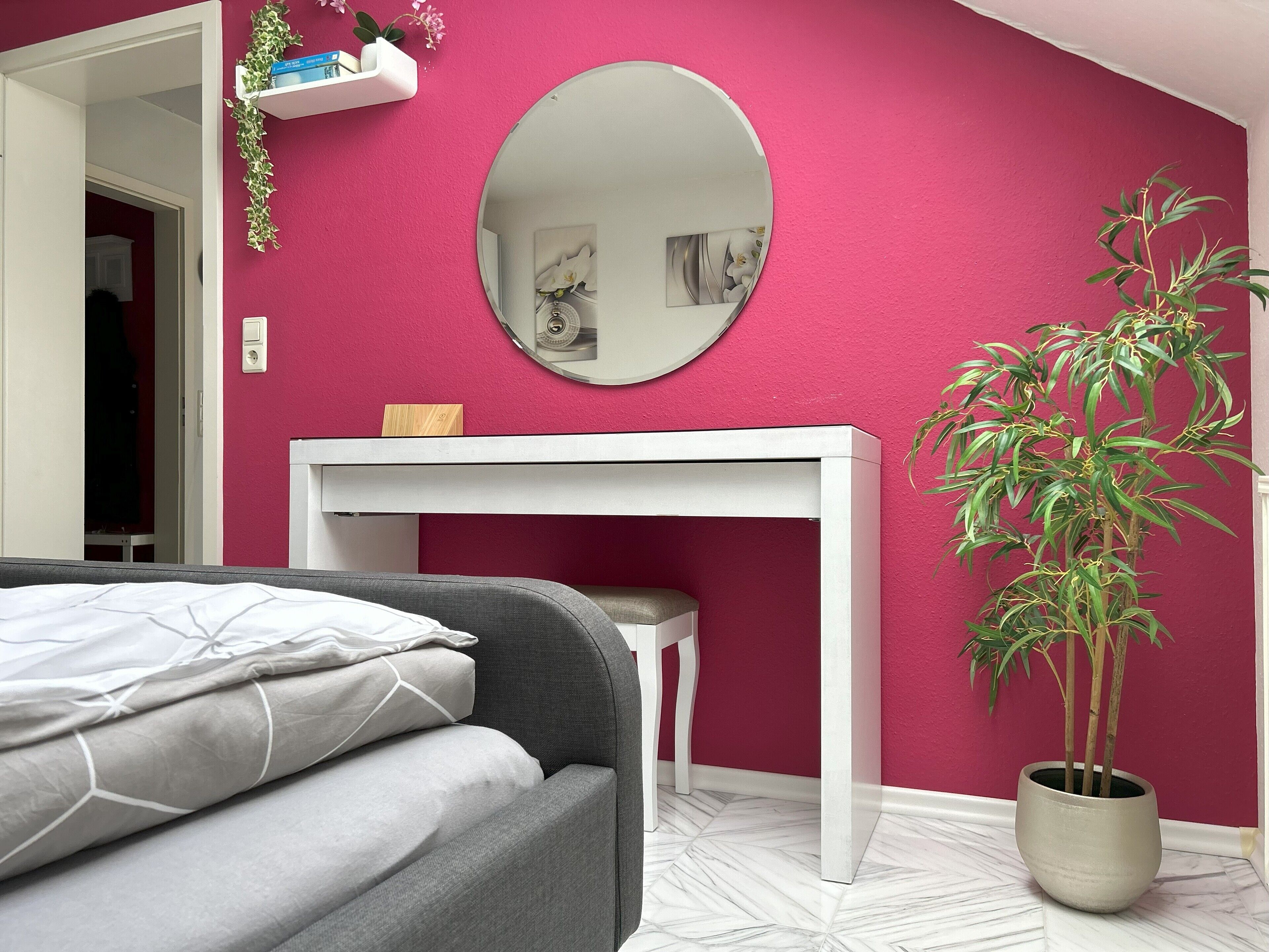A bedroom with a bed, a desk, a mirror, and a potted plant.