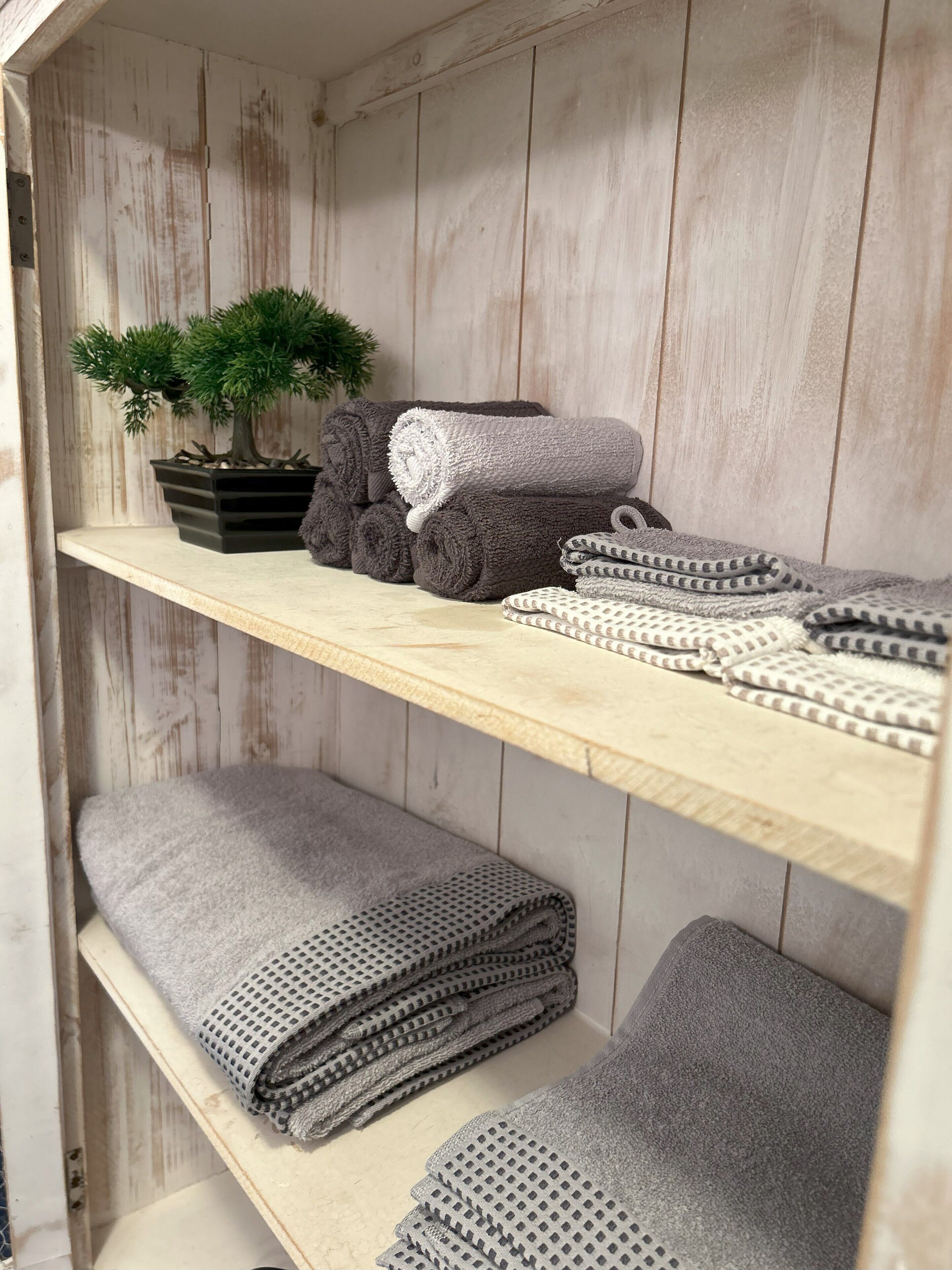 A wooden shelf with neatly folded towels and a potted plant.