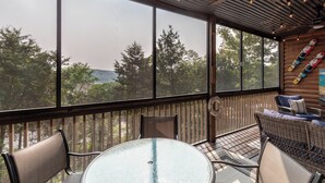 A covered outdoor seating area with a glass table and chairs, large windows offering a view of trees and hills, and a wooden wall with skis. - 1BR Village At Indian Point 1303 near SDC-Free Tickets Daily up to $500 Value (Branson)
