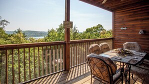 Eine Holzterrasse mit Tisch und Stühlen mit Blick auf einen See und Hügel.