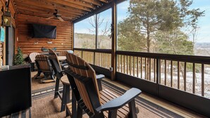 Una terrazza in legno con poltrone Adirondack e un tavolo, una ventola a soffitto e un televisore montato a parete.