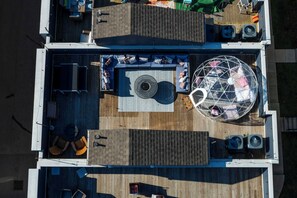 An aerial view of a deck with seating areas, a central circular rug, and a spherical structure. - Dolly's Rooftop Igloo (Nashville)