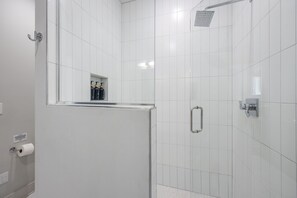 A modern bathroom with white tiles, a glass shower enclosure, a toilet paper holder, and a handrail. - Dolly's Rooftop Igloo (Nashville)