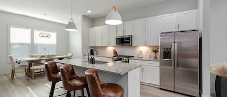Una cocina moderna con armarios blancos, electrodomésticos de acero inoxidable y una isla central con taburetes de bar.