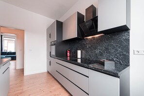 A modern kitchen with grey cabinetry, a black marble countertop, and a built-in oven.