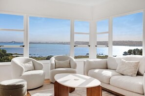 Een ruime kamer met een groot erkerraam met uitzicht op een waterpartij en een verre skyline.